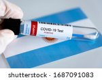Testing for presence of coronavirus in Argentina. Tube containing a swab sample that has tested positive for COVID-19. Argentinian flag in the background.