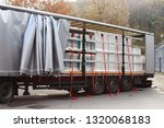 Small photo of Side view of a opened truck trailer in front of a warehouse loaded with pallets with various wrapped plastic goods. Grey side curtain is open and red ratchet tie down straps are hanging on the side.