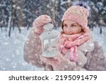 A happy woman stands with a lantern in her hands, a winter park with snow-covered trees