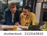 Small photo of Two diverse natural colleagues in casual office or home office doing paperwork working together teaching, coaching or tutoring each other one another