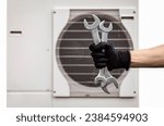 Small photo of Heat Pump Installation and Maintenance Service concept. Craftsman Hand with Tools in front of Thermal Air Heat Pump. Modern Heating Home. Efficient and Renewable Source of Energy.
