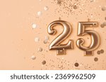 Gold candles in the form of number twenty five on peach background with confetti. 25 years anniversary celebration.