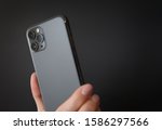 Person holding modern smartphone with triple-lens camera against dark background