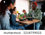 Young multiracial parents and their son eats lunch in a van they live in. African father is feeding his son, who sits on his Asian mother