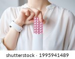 Small photo of Unrecognized woman in white blouse holding hormonal oral contraceptives in a pink blister. Concept of Hormonal methods of birth control. Estrogen and Progestin hormonal balance.