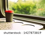 A paper coffee cup with a red plastic lid and a white inscription circle. Coffee to go on a table in the train overlooking a beautiful rural green landscape. Travel, lifestyle