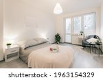 Small photo of Modern bedroom in simple design with prepared bottle of wine and two glasses.White and gray predominate in room.Space is decorated with plants of various kinds.In corner is armchair with reading lamp.