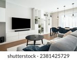 Modern living room with dining area in clean design with builtin furniture and window.There're large TV with sound bar,coffee table,many decorative plants,massive table with chairs and ceiling lights.
