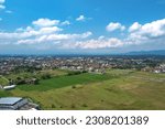 A panoramic view of the city of Purwokerto captured from above with a wide lens, showing the hustle and bustle of the city center. The background features settlements and vacant land.