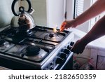 A man's hand with a match lights a gas burner or a gas stove in the kitchen.