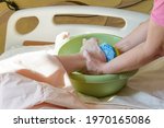 Small photo of Washing the feet of a bedridden patient. The nurse washes the leg over the basin with a washcloth with soapy foam. Concept of caring for a bedridden patient with dementia, stroke.