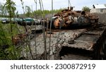 A wrecked, destroyed, burned rusty tank stands in the bushes. The muzzle of the tank is directed at the road. Russian-Ukrainian War 2022-2023