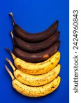 Small photo of Rotten bananas on a blue background from above. Bananas that are beginning to spoil and bananas that have already spoiled. Yellow and black spoiled bananas. Food waste. Spoiled fruits.