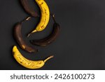 Small photo of Rotten bananas on a black background from above. Bananas that are beginning to spoil and bananas that have already spoiled. Yellow and brown spoiled bananas. Food waste.
