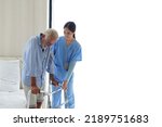 Smiling nurse assisting senior man to get up from bed. Caring nurse supporting patient while getting up from bed and move towards walker at home. Helping elderly disabled man standing up
