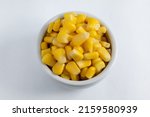 Small portion of sweet corn kernels, cooked and preserved, inside a small ceramic bowl. On white background.