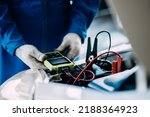 Small photo of close up view of automotive mechanics repairman using a digital battery tester to check and analyze the battery in the car, check the mileage of the car, auto maintenance service concept.