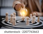 close up of businesswomen holding bulb light center point on dart board with wooden peg dolls, teamwork, competitive, success, goals, strategy, partnership, business solution concept.