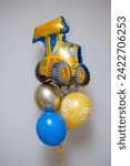 Small photo of A yellow box with balloons, a gold balloon number 2, a foil tractor balloon, the inscription on the balloon “Happy Birthday,” the inscription on the box: “Happy Birthday, son!” Balloons for a boy for