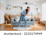 Small photo of House cleaning with fun. Happy young asian housewife singing her favorite song during cleanup, using mop as microphone, enjoying domestic work. Young woman dancing and cleaning in living room