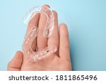 Close up mans hand holding invisible aligners for whitening and straightening of teeth on the blue background. Orthodontic therapy after brackets. Teeth healthcare