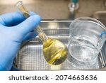 Small photo of Scientist in blue rubber puts a yellow solution in the flask and beaker for dissolving or extraction into ultrasound bath. Urea analysis. Clinical, toxicological and forensic analysis.