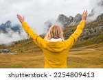 Happy woman spreads hands and sees Passo Giau pass in dense fog. Young traveler smiles standing in Italian Alps 