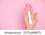 Female hand holding a negative pregnancy test on the pink background with copy space. 