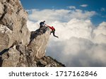 Small photo of Male climber reaching out to help his friend get over the cliffs edge