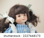 Vintage porcelain doll girl with brown eyes brunette with braided ribbons in a blue dress with white vertical stripes and a lace apron. 