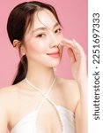 Small photo of Young Asian woman gathered in ponytail with natural makeup on face have plump lips and clean fresh skin wearing white camisole on isolated pink background. Portrait of cute female model in studio.