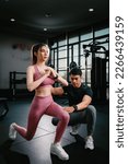 Small photo of Young slim fitness Asian woman standing with a towel near personal trainer help her doing squat legs in the gym. The athlete leads a healthy lifestyle. Cardio training for weight loss.