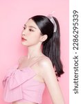 Small photo of Cute Asian woman model gathered in ponytail with korean makeup style on face have plump lips and clean fresh skin wearing pink camisole on isolated pink background.