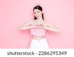 Small photo of Cute Asian woman model gathered in ponytail with korean makeup style on face have plump lips and clean fresh skin wearing pink camisole show heart sign on isolated pink background.