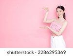 Small photo of Cute Asian woman model gathered in ponytail with korean makeup style on face have plump lips and clean fresh skin wearing pink camisole present left copy space on isolated pink background.