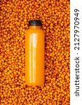 Small photo of Sea buckthorn juice in a transparent plastic bottle against the background of frozen yellow sea buckthorn berries