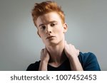 Small photo of Cutie pie. Handsome humourless red-haired young man wearing a t-shirt and staring and touching his neck