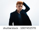 Small photo of Hottie. Attractive stern red-headed young man wearing a black jacket and touching his hair and looking in the distance