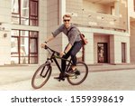 Small photo of Happy manhood. Delighted man keeping smile on his face while riding his bicycle