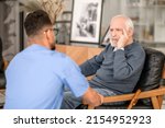 Small photo of Despondent pensioner seated in the room before his caretaker