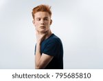 Small photo of Preoccupied. Handsome humourless red-headed young man touching his neck and wearing a black T-shirt and thinking