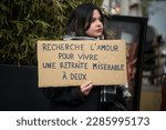 Small photo of Mulhouse - France - 6 April 2023 - woman protesting with placard in french : cherche l'amour pour vivre une retraite miserable a deux, in english, looking for love to live a miserable retirement