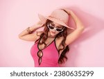 Small photo of An Asian woman exuding beauty poses isolated against a pastel pink backdrop. As a young adult, dressed in summer attire, hinting at an impending travel escapade
