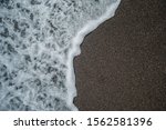 Small photo of Small frothy waves impinge on the black beach of Santorini.