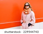 Beauty, fashion, shopping and people concept - pretty stylish woman in coat and sunglasses posing outdoors against colorful wall in the city