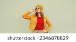Small photo of Autumn style outfit, beautiful stylish young woman looking away wearing orange french beret hat, jacket and round sunglasses on gray background