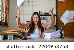 Small photo of Angered, furious, crazy and mad millennial Asian businesswoman or female office worker screaming, shouting and throwing up papers at her office desk. Depression, overworked, failure.