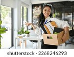 Small photo of Smiling and cheerful millennial Asian female office worker, carrying a cardboard box with her stuff, celebrating her resignation, happy to quit her job.