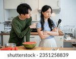 Small photo of A cute, clingy young Asian boyfriend is asking for forgiveness from his unhappy girlfriend after arguing while cooking in the kitchen together. sulky girlfriend and clingy boyfriend