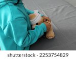 4-year-old brunette Latina girl with glasses represents mistreatment and physical abuse in her teddy bear with bandages on her head, she cares for him and heals his wounds